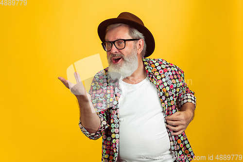 Image of Senior hipster man wearing eyeglasses posing on yellow background. Tech and joyful elderly lifestyle concept