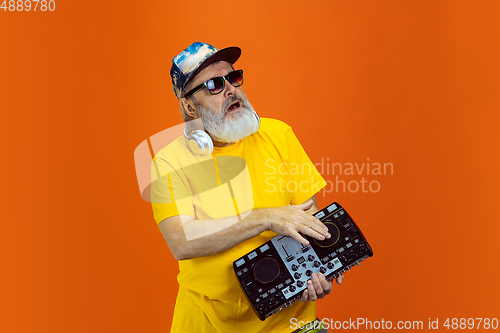 Image of Senior hipster man using devices, gadgets on orange background. Tech and joyful elderly lifestyle concept