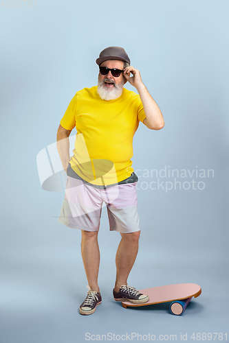 Image of Senior hipster man wearing eyeglasses posing on light blue background. Tech and joyful elderly lifestyle concept