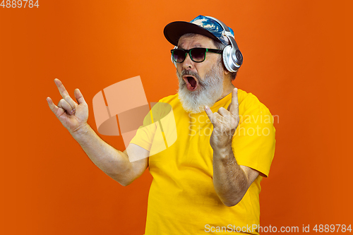 Image of Senior hipster man using devices, gadgets on orange background. Tech and joyful elderly lifestyle concept