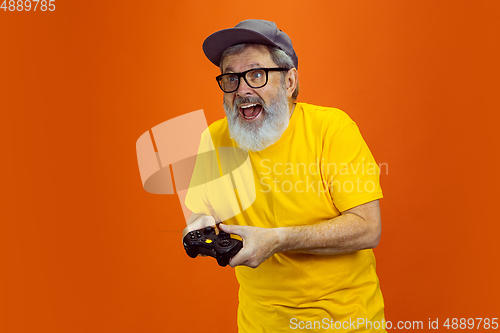 Image of Senior hipster man using devices, gadgets on orange background. Tech and joyful elderly lifestyle concept