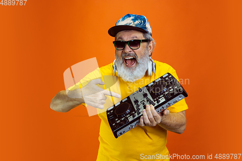 Image of Senior hipster man using devices, gadgets on orange background. Tech and joyful elderly lifestyle concept