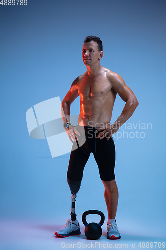 Image of Athlete with disabilities or amputee isolated on blue studio background. Professional male sportsman with leg prosthesis training with weights in neon