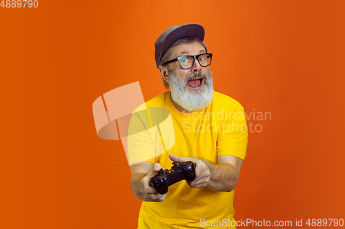 Image of Senior hipster man using devices, gadgets on orange background. Tech and joyful elderly lifestyle concept