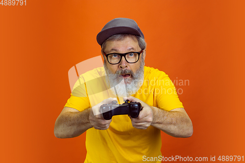 Image of Senior hipster man using devices, gadgets on orange background. Tech and joyful elderly lifestyle concept