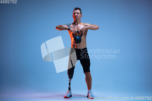 Image of Athlete with disabilities or amputee isolated on blue studio background. Professional male sportsman with leg prosthesis training with weights in neon