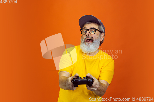 Image of Senior hipster man using devices, gadgets on orange background. Tech and joyful elderly lifestyle concept