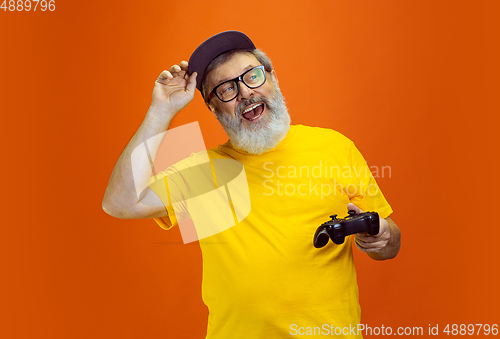 Image of Senior hipster man using devices, gadgets on orange background. Tech and joyful elderly lifestyle concept