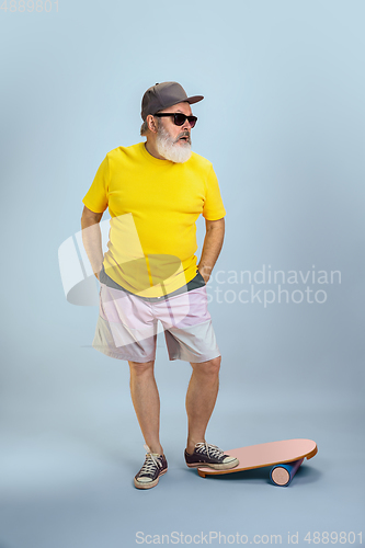 Image of Senior hipster man wearing eyeglasses posing on light blue background. Tech and joyful elderly lifestyle concept