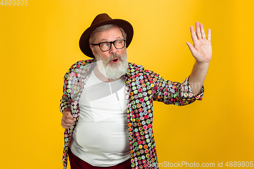 Image of Senior hipster man wearing eyeglasses posing on yellow background. Tech and joyful elderly lifestyle concept