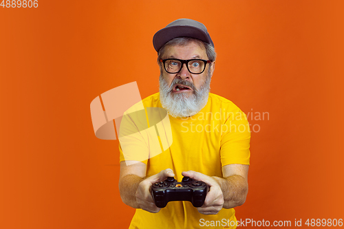 Image of Senior hipster man using devices, gadgets on orange background. Tech and joyful elderly lifestyle concept