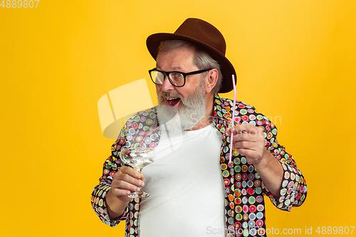 Image of Senior hipster man wearing eyeglasses posing on yellow background. Tech and joyful elderly lifestyle concept