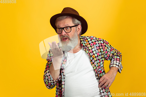 Image of Senior hipster man wearing eyeglasses posing on yellow background. Tech and joyful elderly lifestyle concept