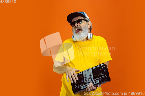 Image of Senior hipster man using devices, gadgets on orange background. Tech and joyful elderly lifestyle concept