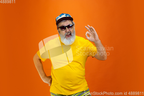 Image of Senior hipster man wearing eyeglasses posing on orange background. Tech and joyful elderly lifestyle concept