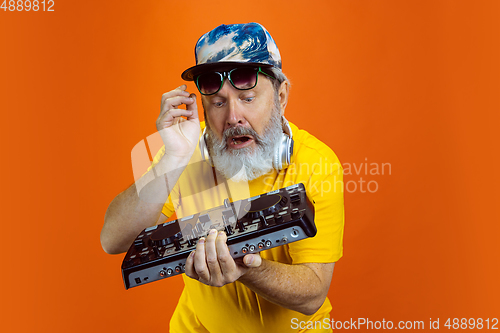 Image of Senior hipster man using devices, gadgets on orange background. Tech and joyful elderly lifestyle concept