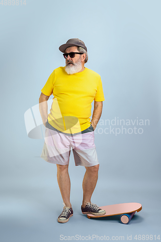 Image of Senior hipster man wearing eyeglasses posing on light blue background. Tech and joyful elderly lifestyle concept
