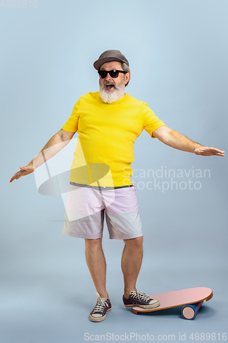 Image of Senior hipster man wearing eyeglasses posing on light blue background. Tech and joyful elderly lifestyle concept