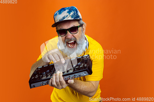 Image of Senior hipster man using devices, gadgets on orange background. Tech and joyful elderly lifestyle concept