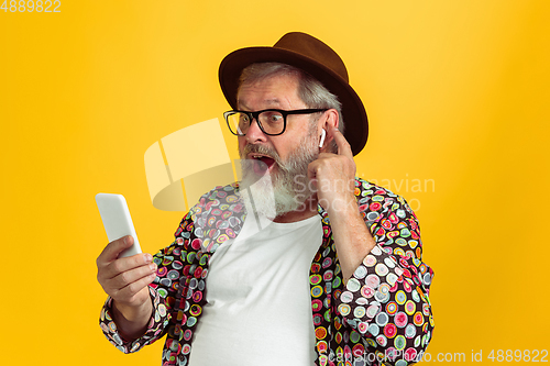 Image of Senior hipster man wearing eyeglasses posing on yellow background. Tech and joyful elderly lifestyle concept