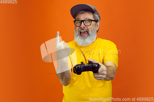 Image of Senior hipster man using devices, gadgets on orange background. Tech and joyful elderly lifestyle concept