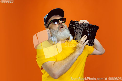 Image of Senior hipster man using devices, gadgets on orange background. Tech and joyful elderly lifestyle concept