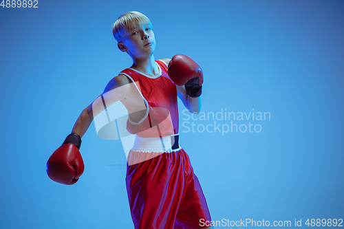 Image of Teenager in sportswear boxing isolated on blue studio background in neon light