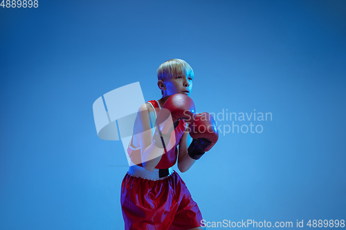 Image of Teenager in sportswear boxing isolated on blue studio background in neon light