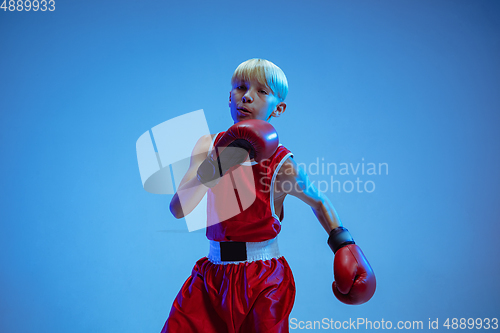 Image of Teenager in sportswear boxing isolated on blue studio background in neon light