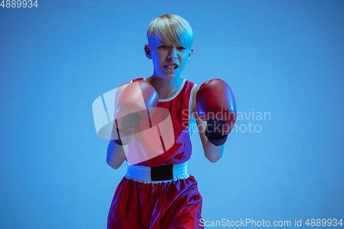 Image of Teenager in sportswear boxing isolated on blue studio background in neon light