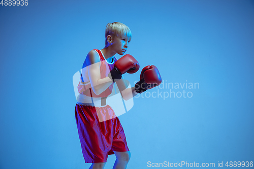 Image of Teenager in sportswear boxing isolated on blue studio background in neon light