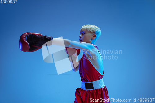 Image of Teenager in sportswear boxing isolated on blue studio background in neon light