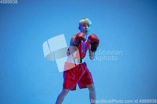Image of Teenager in sportswear boxing isolated on blue studio background in neon light