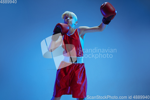 Image of Teenager in sportswear boxing isolated on blue studio background in neon light