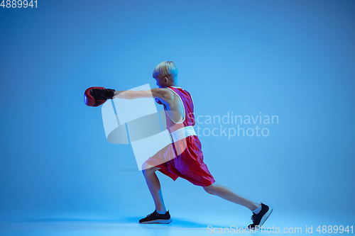 Image of Teenager in sportswear boxing isolated on blue studio background in neon light
