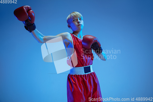 Image of Teenager in sportswear boxing isolated on blue studio background in neon light