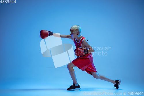Image of Teenager in sportswear boxing isolated on blue studio background in neon light