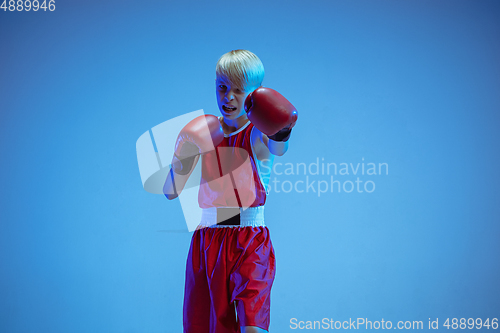 Image of Teenager in sportswear boxing isolated on blue studio background in neon light