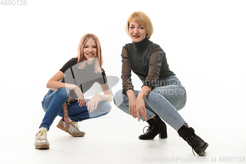 Image of Mother and teenage daughter sat on their knees and cheerfully look into the frame