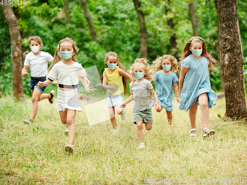 Image of Happy little caucasian kids jumping and running on the meadow, in forest