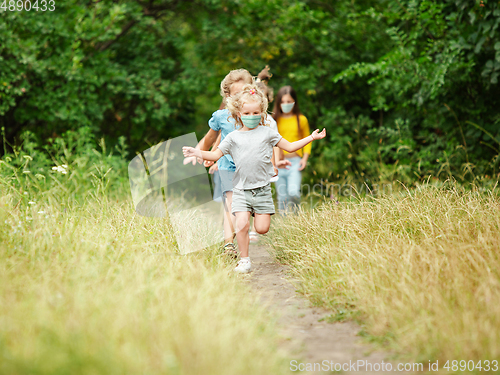 Image of Happy little caucasian kids jumping and running on the meadow, in forest