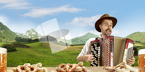 Image of The happy smiling man with beer dressed in traditional Austrian or Bavarian costume holding mug of beer, mountains on background, flyer