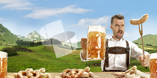 Image of The happy smiling man with beer dressed in traditional Austrian or Bavarian costume holding mug of beer, mountains on background, flyer