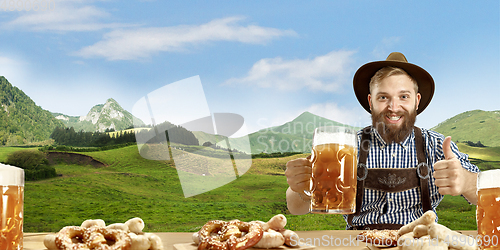 Image of The happy smiling man with beer dressed in traditional Austrian or Bavarian costume holding mug of beer, mountains on background, flyer