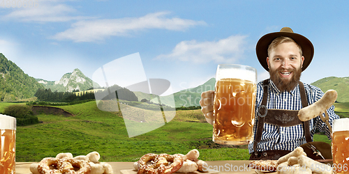 Image of The happy smiling man with beer dressed in traditional Austrian or Bavarian costume holding mug of beer, mountains on background, flyer