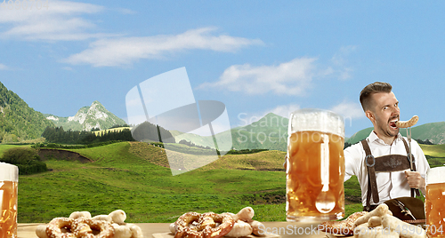 Image of The happy smiling man with beer dressed in traditional Austrian or Bavarian costume holding mug of beer, mountains on background, flyer