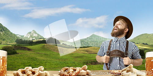 Image of The happy smiling man with beer dressed in traditional Austrian or Bavarian costume holding mug of beer, mountains on background, flyer