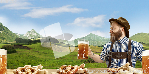 Image of The happy smiling man with beer dressed in traditional Austrian or Bavarian costume holding mug of beer, mountains on background, flyer