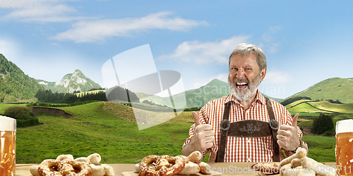 Image of The senior happy smiling man with beer dressed in traditional Austrian or Bavarian costume holding mug of beer, mountains on background, flyer