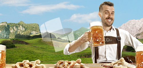 Image of The happy smiling man with beer dressed in traditional Austrian or Bavarian costume holding mug of beer, mountains on background, flyer